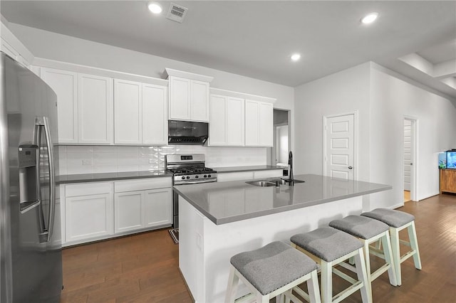 kitchen featuring visible vents, stainless steel appliances, tasteful backsplash, a sink, and dark wood-style floors