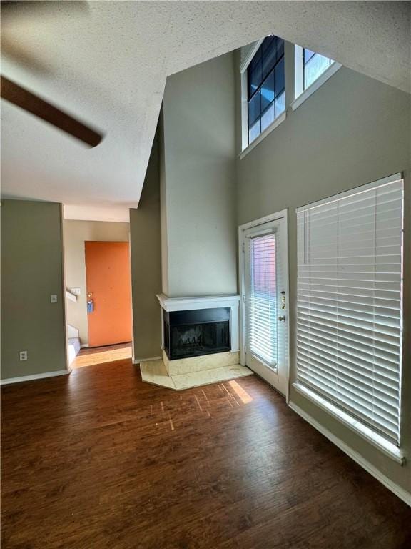 unfurnished living room with a high ceiling, a textured ceiling, ceiling fan, and dark wood-type flooring