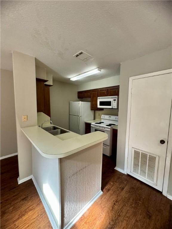 kitchen with dark brown cabinetry, sink, dark hardwood / wood-style floors, kitchen peninsula, and white appliances