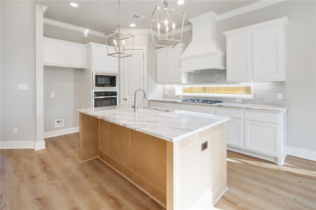 kitchen with white cabinets, custom range hood, a kitchen island with sink, and appliances with stainless steel finishes