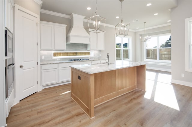 kitchen featuring custom range hood, white cabinetry, a kitchen island with sink, and light stone counters