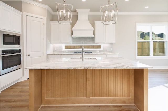 kitchen featuring white cabinetry, custom range hood, stainless steel appliances, and a kitchen island with sink