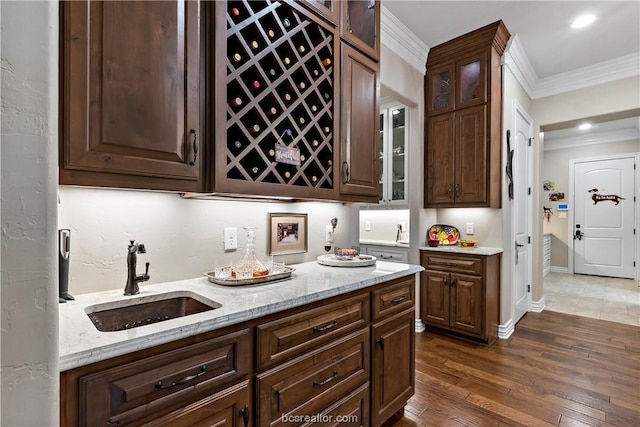 bar featuring dark brown cabinetry, sink, light stone counters, dark hardwood / wood-style flooring, and ornamental molding