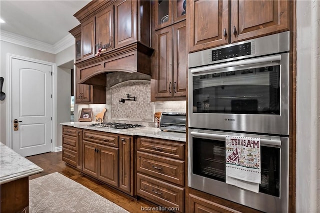 kitchen with custom exhaust hood, crown molding, tasteful backsplash, light stone counters, and stainless steel appliances