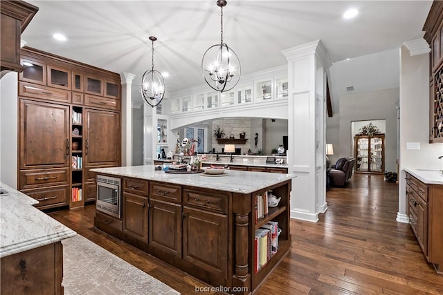 kitchen with stainless steel microwave, a center island, dark hardwood / wood-style floors, decorative light fixtures, and dark brown cabinets