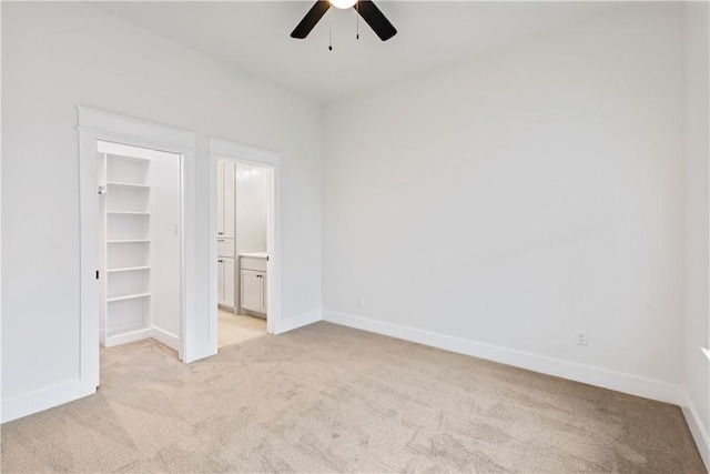 unfurnished bedroom featuring ceiling fan, a spacious closet, light carpet, and a closet