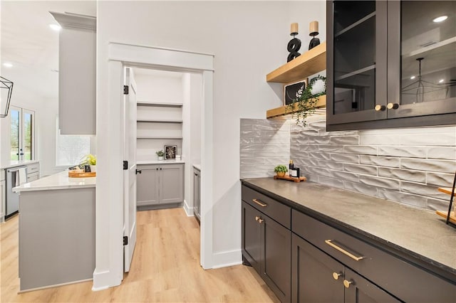 bar with stainless steel dishwasher, decorative backsplash, and light wood-type flooring