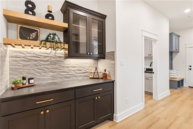 bar featuring dark brown cabinets, tasteful backsplash, sink, and light hardwood / wood-style flooring