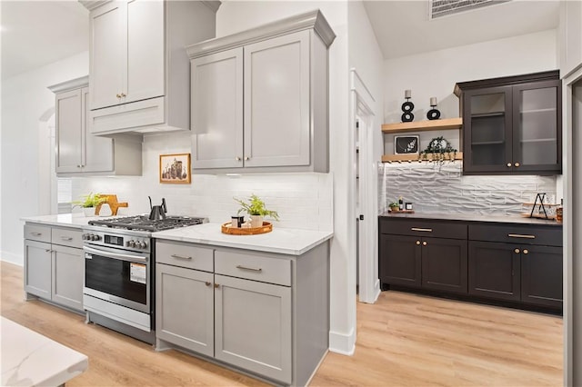 kitchen featuring decorative backsplash, gray cabinets, light wood-type flooring, and stainless steel range