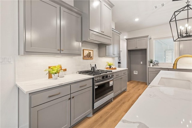 kitchen featuring light stone countertops, sink, light hardwood / wood-style flooring, gray cabinets, and stainless steel stove