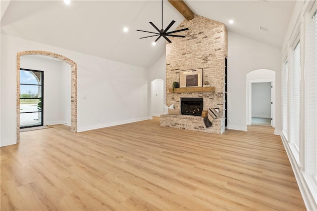 unfurnished living room featuring beam ceiling, ceiling fan, high vaulted ceiling, a fireplace, and light wood-type flooring