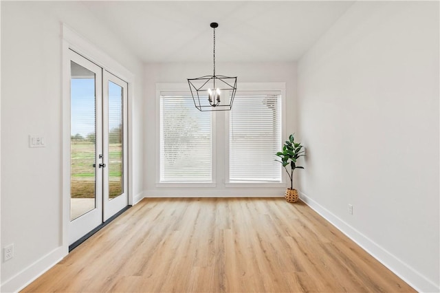 unfurnished dining area featuring light hardwood / wood-style floors, french doors, a wealth of natural light, and an inviting chandelier