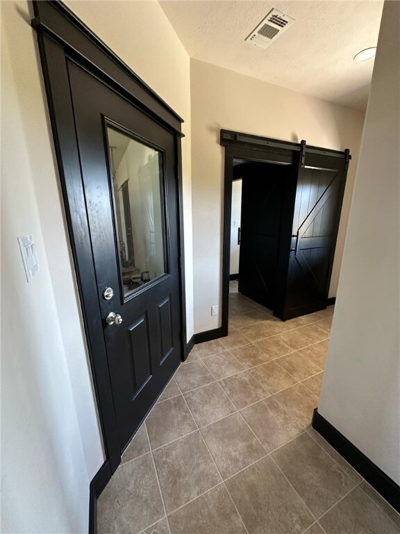 10601 Fm 1179, Bryan, TX 77808 - hall featuring a barn door, baseboards, tile patterned flooring, and a textured ceiling