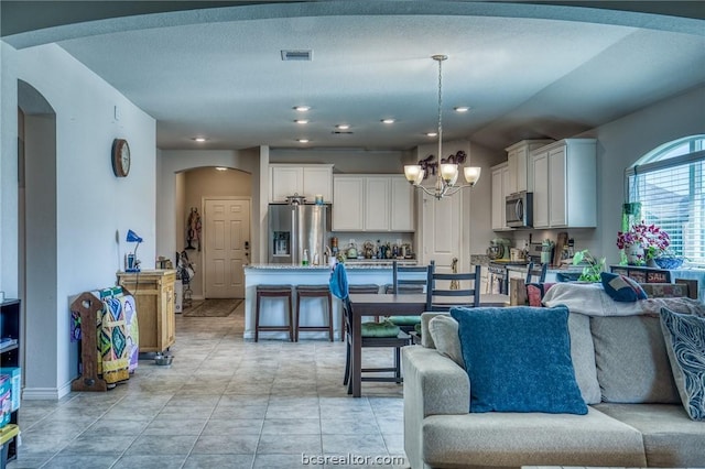 kitchen with appliances with stainless steel finishes, an inviting chandelier, white cabinetry, and pendant lighting