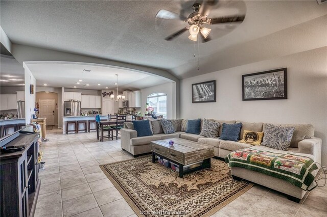 living room with light tile patterned floors, ceiling fan with notable chandelier, and a textured ceiling