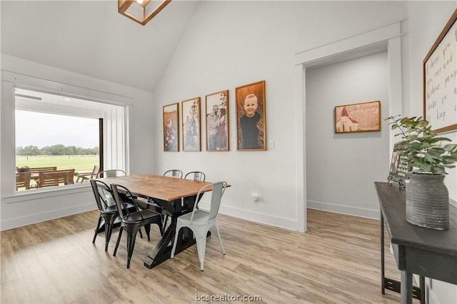 dining room with high vaulted ceiling and light hardwood / wood-style floors