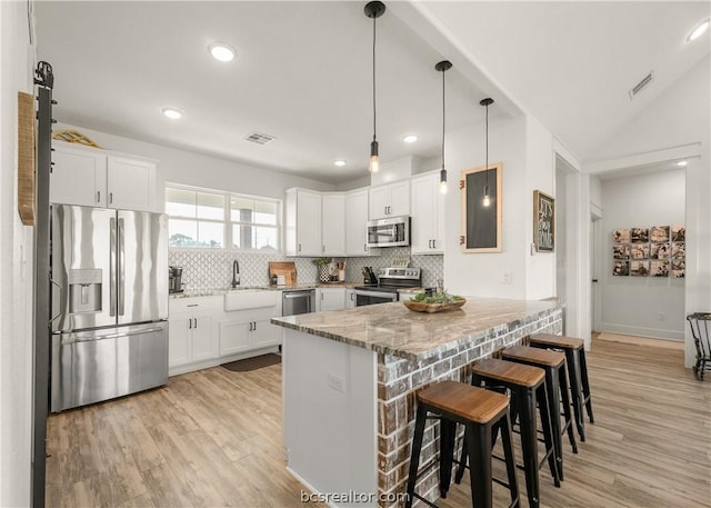 kitchen featuring a kitchen breakfast bar, light hardwood / wood-style flooring, light stone counters, white cabinetry, and stainless steel appliances