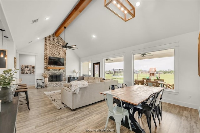 dining room featuring a fireplace, beam ceiling, high vaulted ceiling, and light hardwood / wood-style flooring