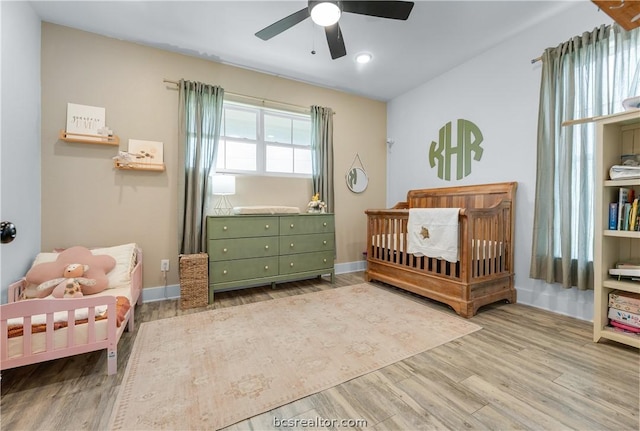 bedroom featuring ceiling fan, light hardwood / wood-style flooring, and a crib