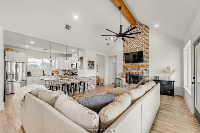 living room featuring vaulted ceiling with beams, ceiling fan, light hardwood / wood-style floors, and a brick fireplace