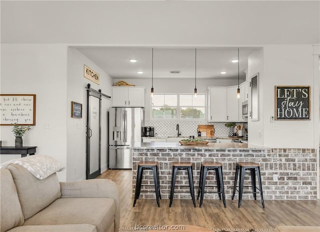 kitchen with white cabinets, a barn door, appliances with stainless steel finishes, light hardwood / wood-style floors, and a kitchen bar