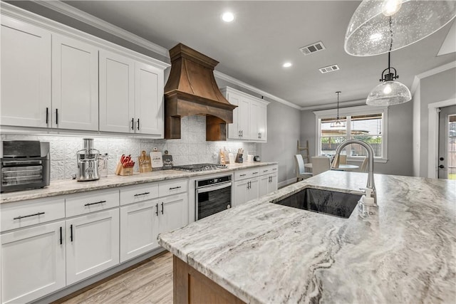 kitchen with sink, custom exhaust hood, white cabinets, and appliances with stainless steel finishes