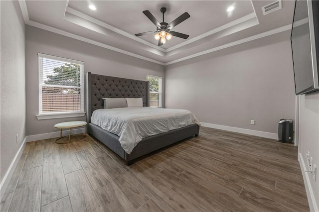 bedroom with crown molding, a tray ceiling, dark hardwood / wood-style floors, and ceiling fan