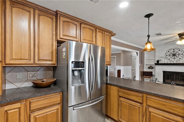 kitchen featuring crown molding, a brick fireplace, stainless steel fridge, pendant lighting, and decorative backsplash