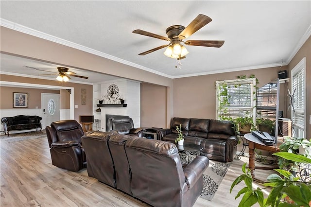 living room featuring crown molding, a fireplace, ceiling fan, and light hardwood / wood-style flooring