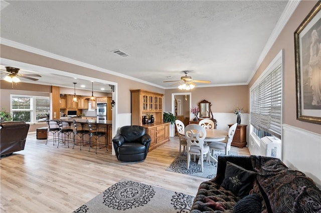 living room featuring crown molding, ceiling fan, a textured ceiling, and light hardwood / wood-style flooring