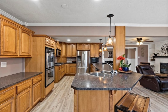 kitchen with appliances with stainless steel finishes, sink, ornamental molding, a kitchen island with sink, and light wood-type flooring