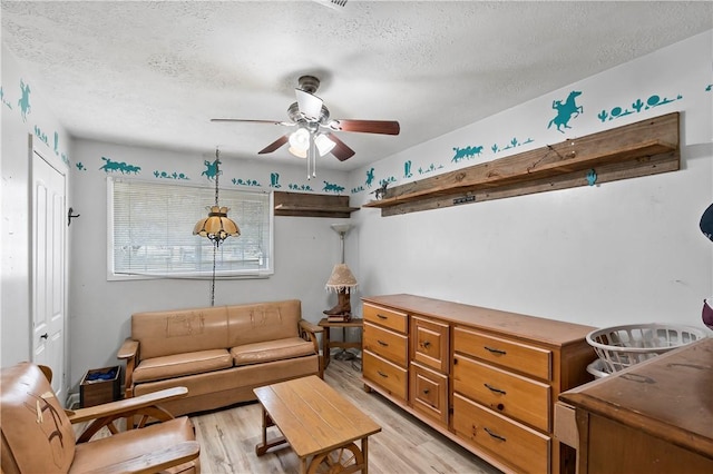 living room featuring ceiling fan, a textured ceiling, and light wood-type flooring