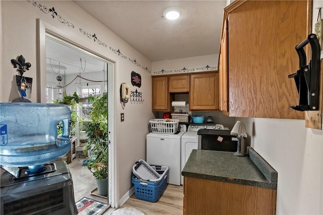 washroom featuring cabinets, a textured ceiling, washing machine and clothes dryer, and light wood-type flooring