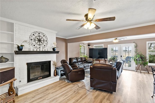 living room with crown molding, light hardwood / wood-style flooring, a fireplace, a textured ceiling, and french doors