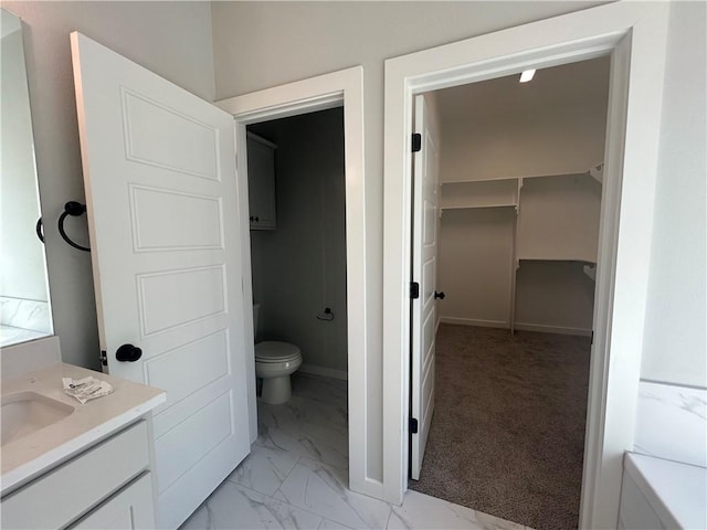 bathroom with toilet, vanity, baseboards, marble finish floor, and a walk in closet