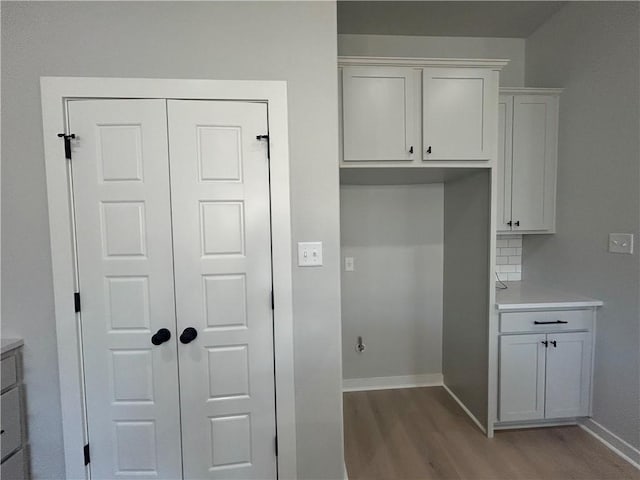 interior space with baseboards, wood finished floors, light countertops, white cabinetry, and backsplash