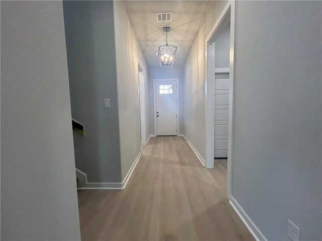 hallway with visible vents, a notable chandelier, light wood-style flooring, and baseboards