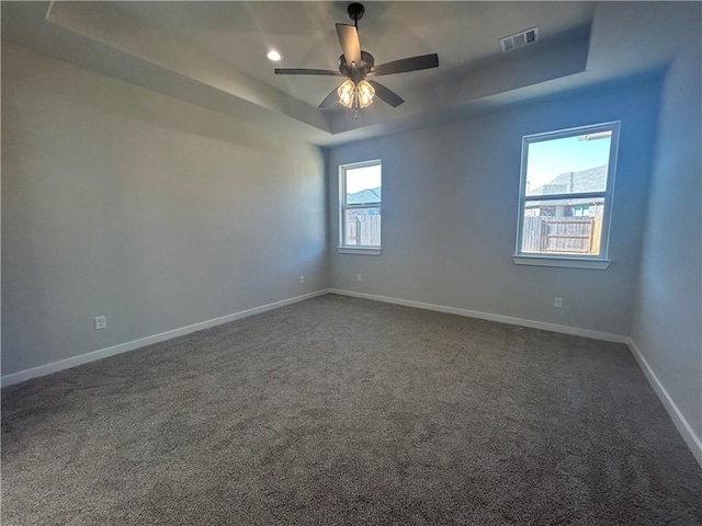 unfurnished room featuring visible vents, baseboards, ceiling fan, a tray ceiling, and dark carpet