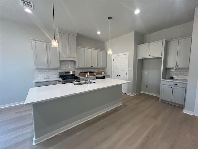 kitchen featuring a center island with sink, visible vents, gas stove, a sink, and baseboards