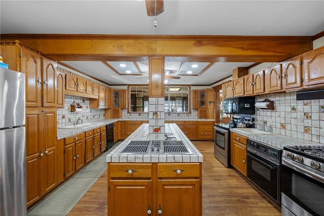 kitchen with backsplash, tile countertops, a kitchen island, and black appliances