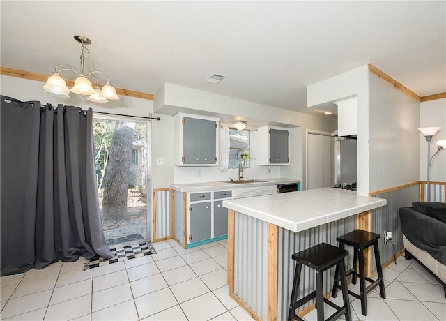 kitchen featuring blue cabinetry, tile counters, a notable chandelier, dishwasher, and hanging light fixtures