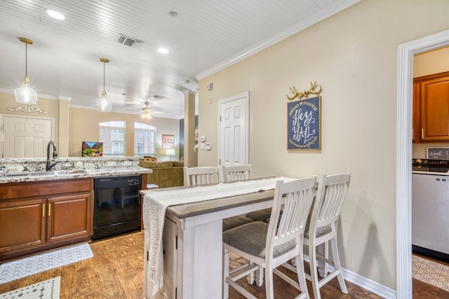 kitchen with black dishwasher, light wood finished floors, hanging light fixtures, a sink, and a kitchen breakfast bar