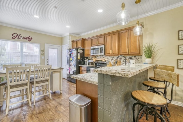 kitchen featuring light stone countertops, appliances with stainless steel finishes, brown cabinets, decorative light fixtures, and crown molding