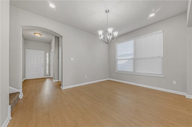 unfurnished room featuring arched walkways, light wood-type flooring, and baseboards