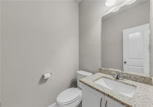 bathroom featuring toilet, vanity, and a textured wall