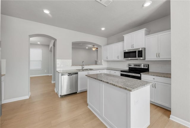 kitchen with a center island, light wood-style floors, arched walkways, stainless steel appliances, and a sink