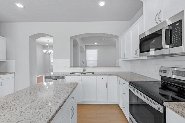 kitchen featuring light stone countertops, a sink, decorative backsplash, white cabinets, and appliances with stainless steel finishes