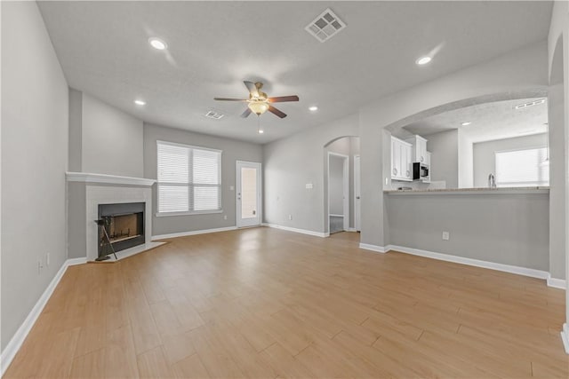 unfurnished living room with visible vents, a fireplace with flush hearth, recessed lighting, light wood-style floors, and a ceiling fan