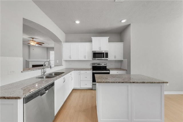 kitchen featuring a ceiling fan, a sink, light stone counters, stainless steel appliances, and light wood-style floors