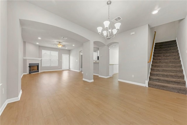 unfurnished living room with visible vents, arched walkways, light wood-style floors, a fireplace, and stairs